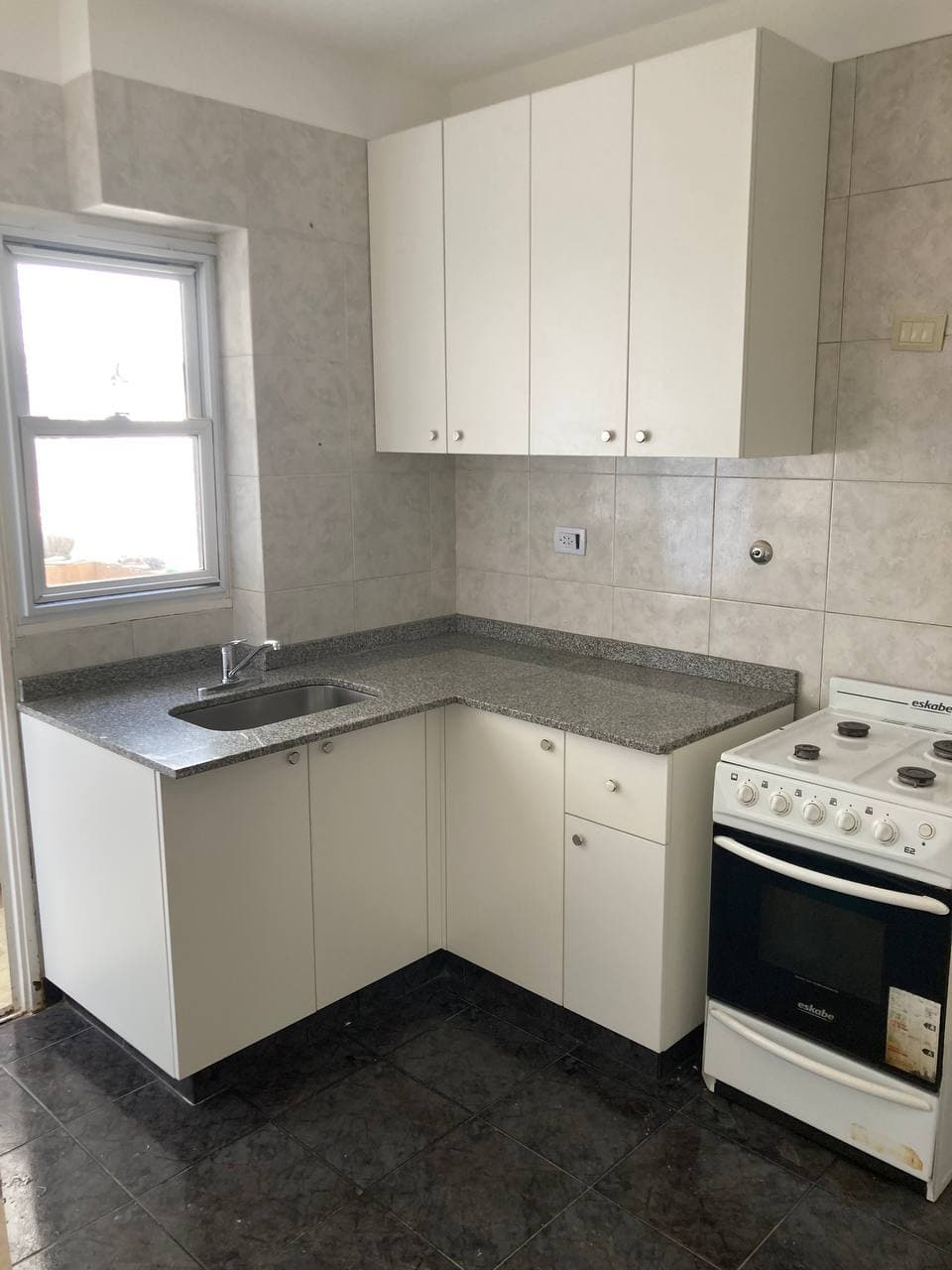 Cocina blanca en esquina con alacenas, bajo mesada y pileta junto a la ventana.