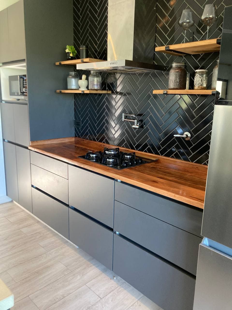Cocina con muebles oscuros, cajones, estantes abiertos y anafe integrado en la mesada.