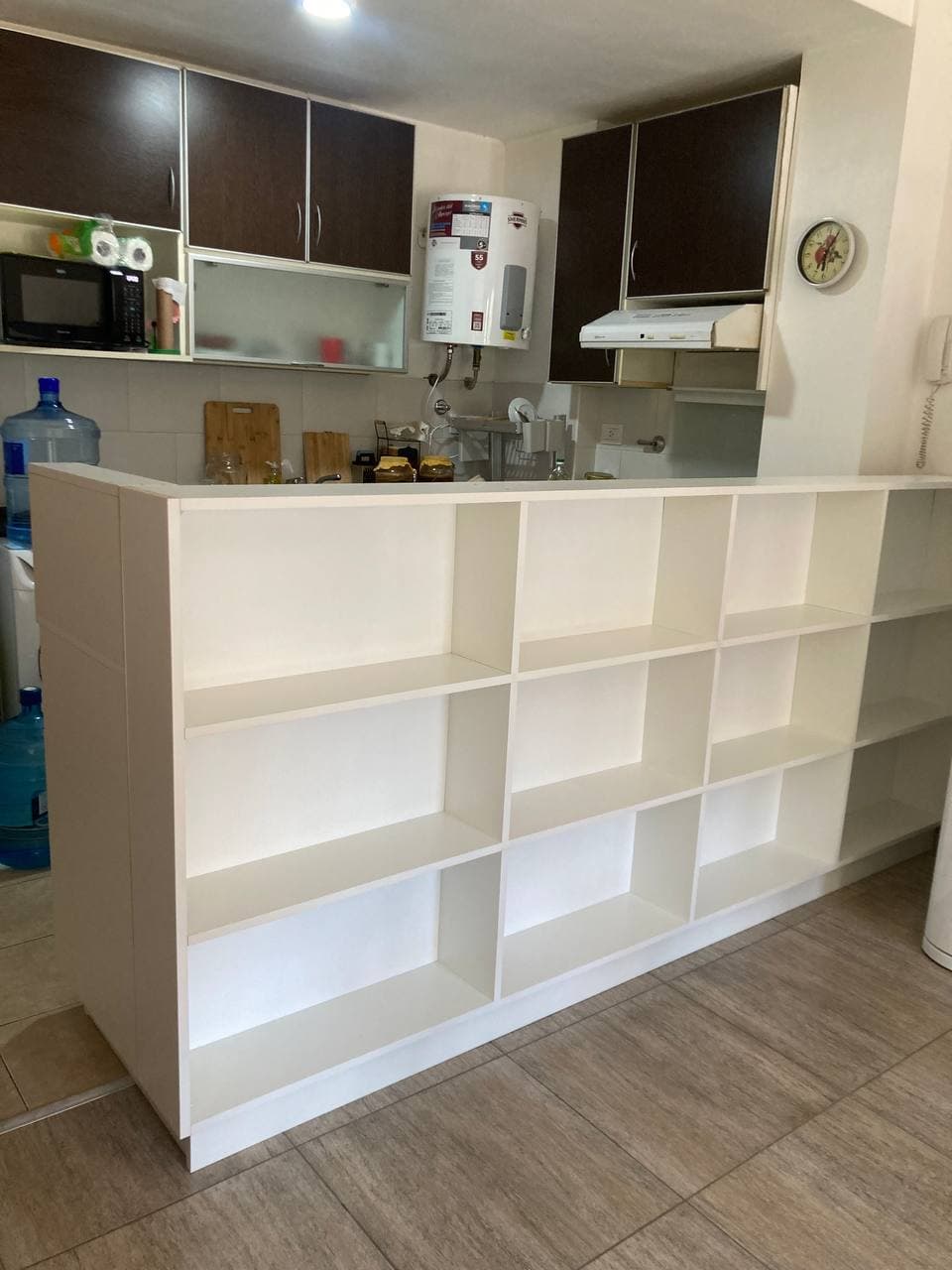 Estantería blanca con compartimentos abiertos que separa la cocina del ambiente contiguo.